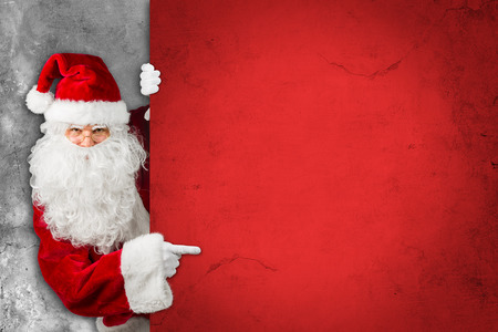 red white classic traditional santa claus looking through behind empty concrecte billboard sign wall pointing finger christmas xmas gift voucher patternの写真素材