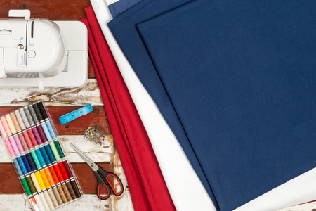 sewing machine blue white red fabric scissors box with colorful cottons measuring tape and pin needles on rustic wooden tableの写真素材