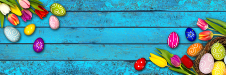 colorful wooden panorama easter background tulips eggs nest basket on rustic old oak light blue wood textureの写真素材