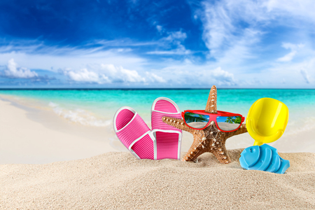 sea star with red sunglasses and beach supplies accessory on sand in front of tropical paradise island dream beachの写真素材
