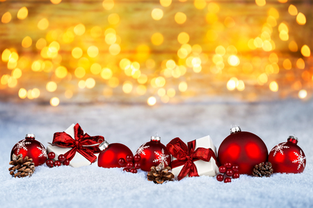 red christmas decoration and white gift presents on snow in front of  bright golden lights bokeh backgroundの写真素材