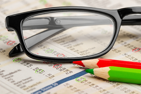 glasses red green pen pencil on newspaper with stock market exchange data chart finance business concept cash backgroundの写真素材