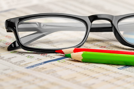 glasses red green pen pencil on newspaper with stock market exchange data chart finance business concept cash backgroundの写真素材