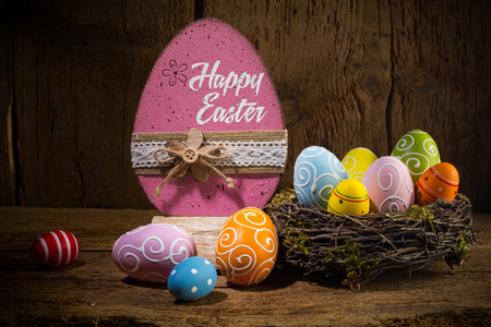 Colorful painted happy easter greeting card eggs in birds nest basket on rustic wooden old  backgroundの写真素材