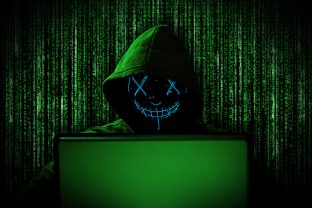 hacker with glowing mask behind notebook laptop in front of green source binary code background internet cyber hack attack computer conceptの写真素材
