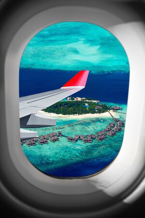 view through airplane window on plane flight wing in front of tropical island in the indian ocean maldive. transportation vacation air travel fly conceptの写真素材