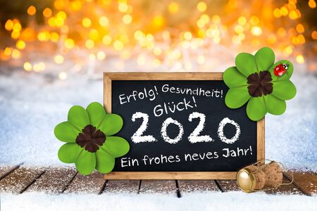 champagne cork and blackboard with german greeting frohes neues jahr 2020 (english translation: happy new year 2020 ) wooden planks in front of bright golden warm bokeh light backgroundの写真素材