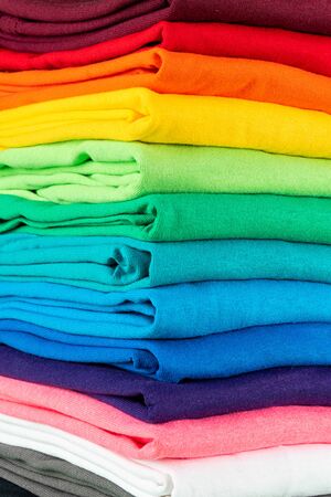 close-up stack of many fresh new fabric cotton t-shirts in colorful rainbow colors. Pile of various colored shirts backgroundの写真素材