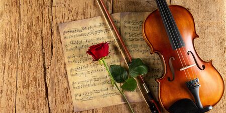 classic retro violin music string instrumt on old music note sheet paper with red rose flower on old oak wood wooden panorama copy space background. classical musical romantic valentines day concept.の写真素材