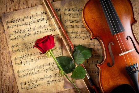 classic retro violin music string instrumt on old music note sheet paper with red rose flower on old oak wood wooden background. classical musical romantic valentines day concept.の写真素材