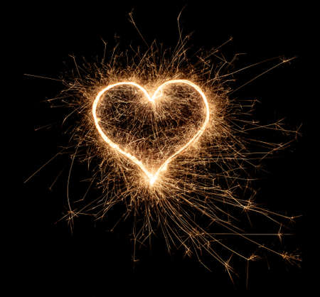 golden bright sparkler heart shape love shaped symbol isolated on dark black background. silvester new year birthday wedding and celebration design patternの写真素材