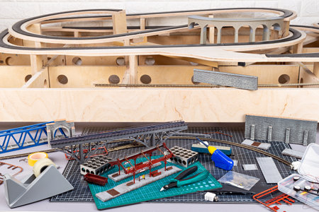 Construction of a model railroad with wooden open frame layout. workbench with model railway train station and landscape tools. Hobby leisure scale modeling conceptの写真素材