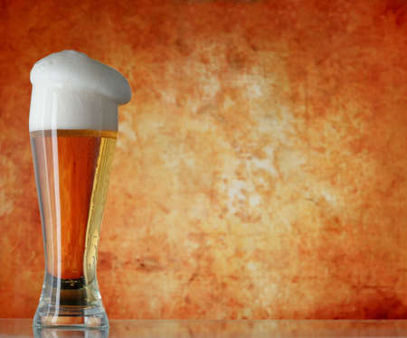 Glass of beer with froth over yellow background の写真素材