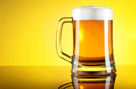 Glass of beer close-up with froth over yellow backgroundの写真素材