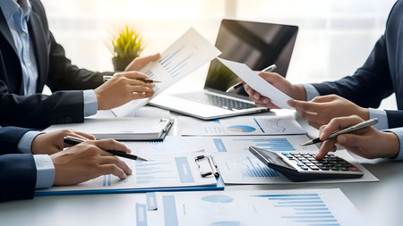 Business team meeting around table reviewing financial report document paperwork and using calculator and laptop computer for analysisの素材