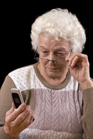 Old woman and the mobile phone isolated in black backgroundの写真素材