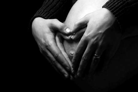 Close-up of a belly with the hands making a heart shape, monocromeの写真素材
