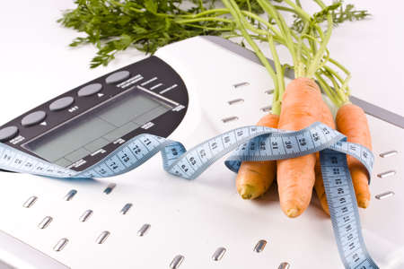 Carrots surrounded by a measuring tape on a white bathroom scale. Blank display. の写真素材
