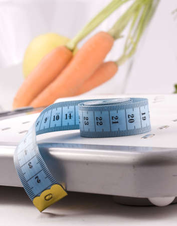 Carrots surrounded by a measuring tape on a white bathroom scale. Blank display. の写真素材