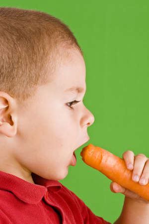 Boy eating fresh carrot isolated on green background の写真素材