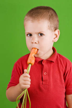 Boy eating fresh carrot on green background の写真素材