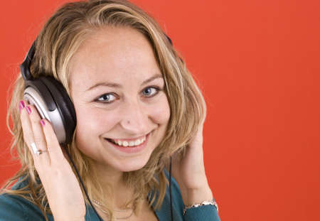 Woman with headphones listening to music and a red background の写真素材