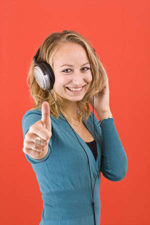Happy woman with headphones, listen to music and showing sign ok. Isolated on red backgroundの写真素材