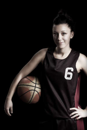 Smiling female basketball player holding ball, in black backgroundの写真素材
