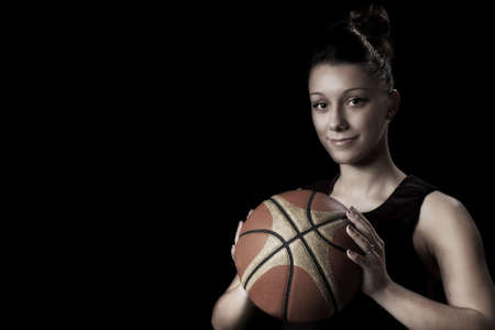 Smiling female basketball player holding ball, in black backgroundの写真素材