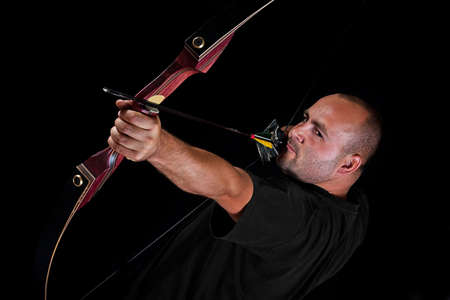 Archer in black on black background aiming with bow and arrow, with focus on eyes. 