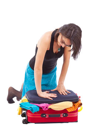 Woman sitting on luggage to close it isolated on white. の写真素材