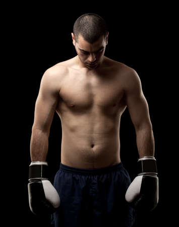 Portrait of a shirtless macho man with boxing gloves against black background の写真素材