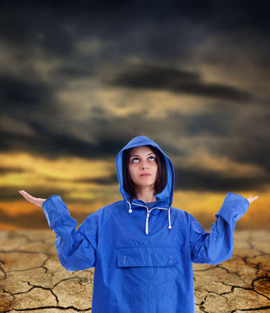 Young woman wears a blue raincoat, waiting for rain, in background apocalyptic sunrise 