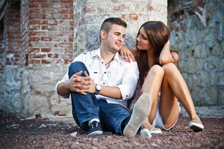 Young couple sitting by brick wall の写真素材
