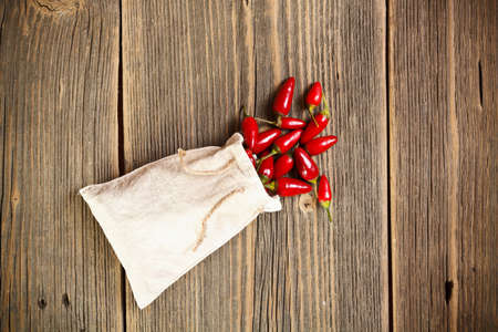 Red chilli peppers in bag on wooden background の写真素材