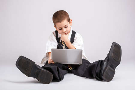 Thoughtful little business boy looking at his laptopの写真素材
