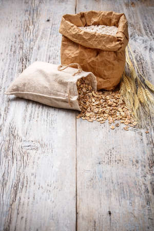 Oat flakes spilling from the burlap bag on old wooden tableの写真素材