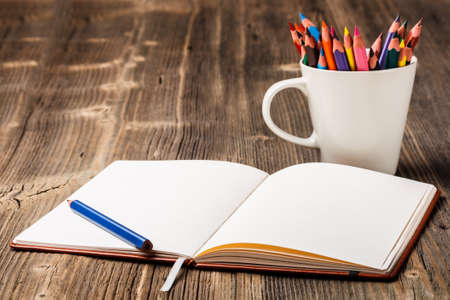 White cup with colorful pencils and notebookの写真素材