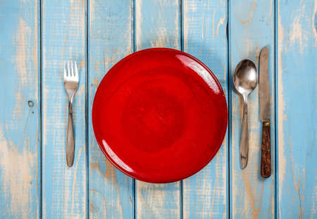 Empty red plate on blue wooden table with knife, spoon and fork の写真素材