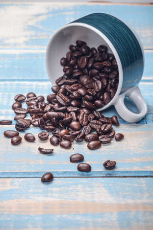 Coffee beans and cup on painted wooden background