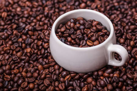 White cup is standing on some coffee beans