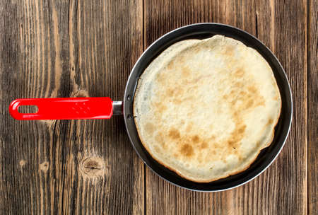 Frying pan with pancake on rustic wooden backgroundの写真素材