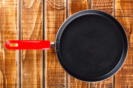 Red frying pan on wooden boardの写真素材
