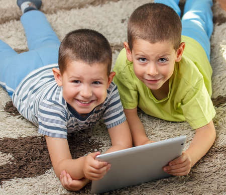 Two kids laying on floor with digital tabletの写真素材