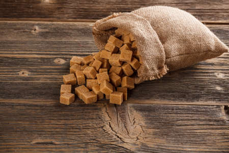 Sugar cubes in burlap sack on wooden backgroundの写真素材