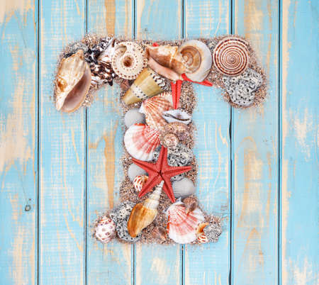 Letter T made of seashell on blue wooden backgroundの写真素材