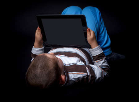 Boy using tablet, lying on the floor, black backgroundの写真素材