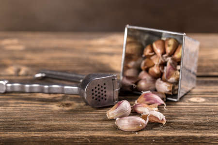 Garlic press  and garlic clove on wooden tableの写真素材