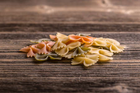 Heap of raw colored pasta farfalle on rustic wooden background