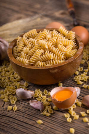 Raw pasta in wooden bowl on wood backgroundの写真素材
